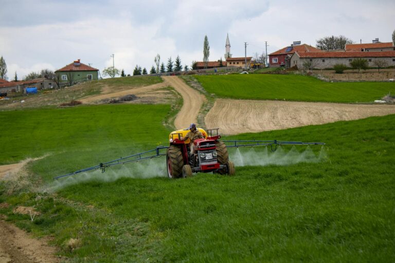 A farmer using a tractor to spray fields in a rural landscape, showcasing agricultural practices.